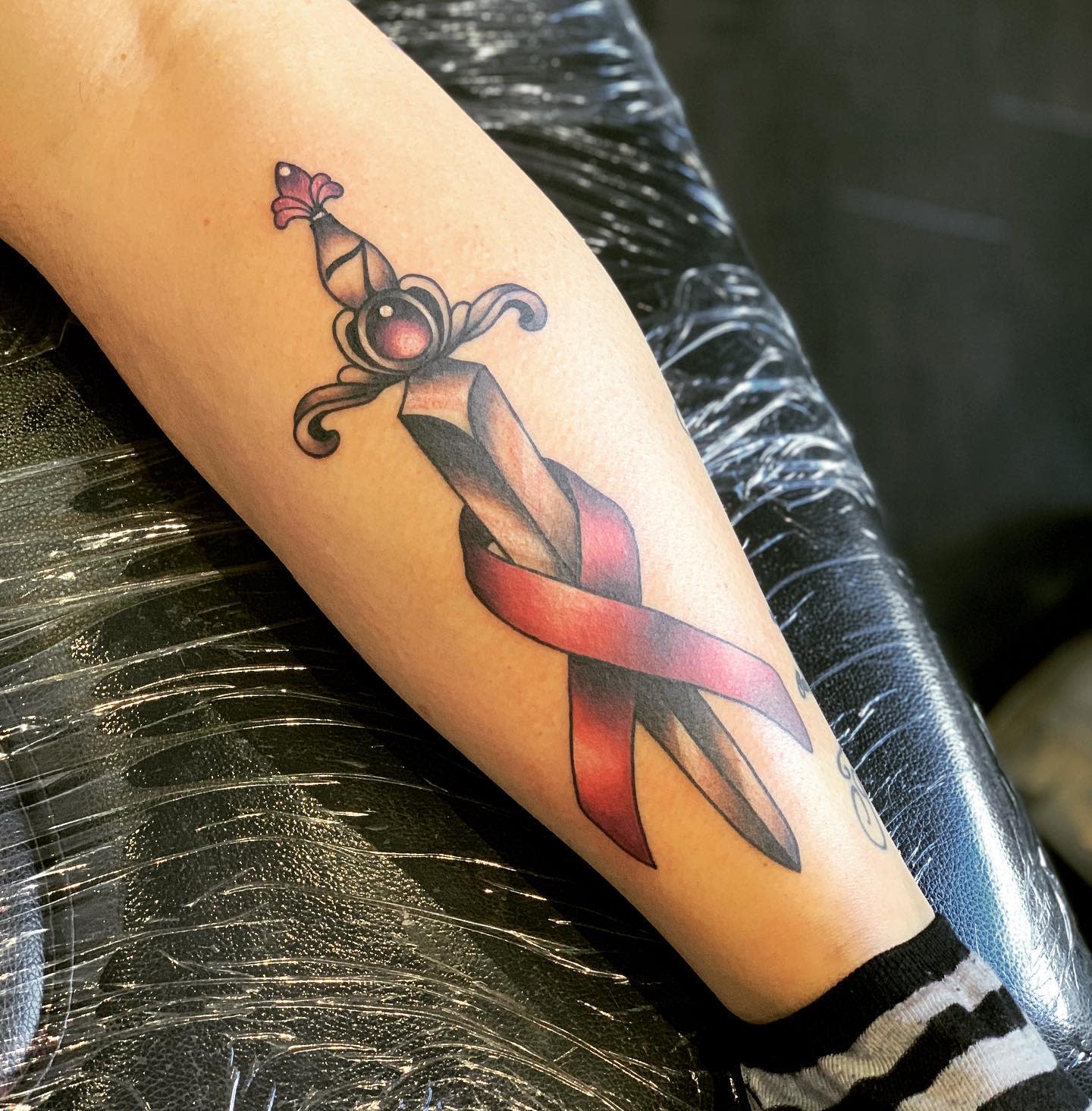 Tattoo of a sword with a red ribbon wrapped around it on a leg